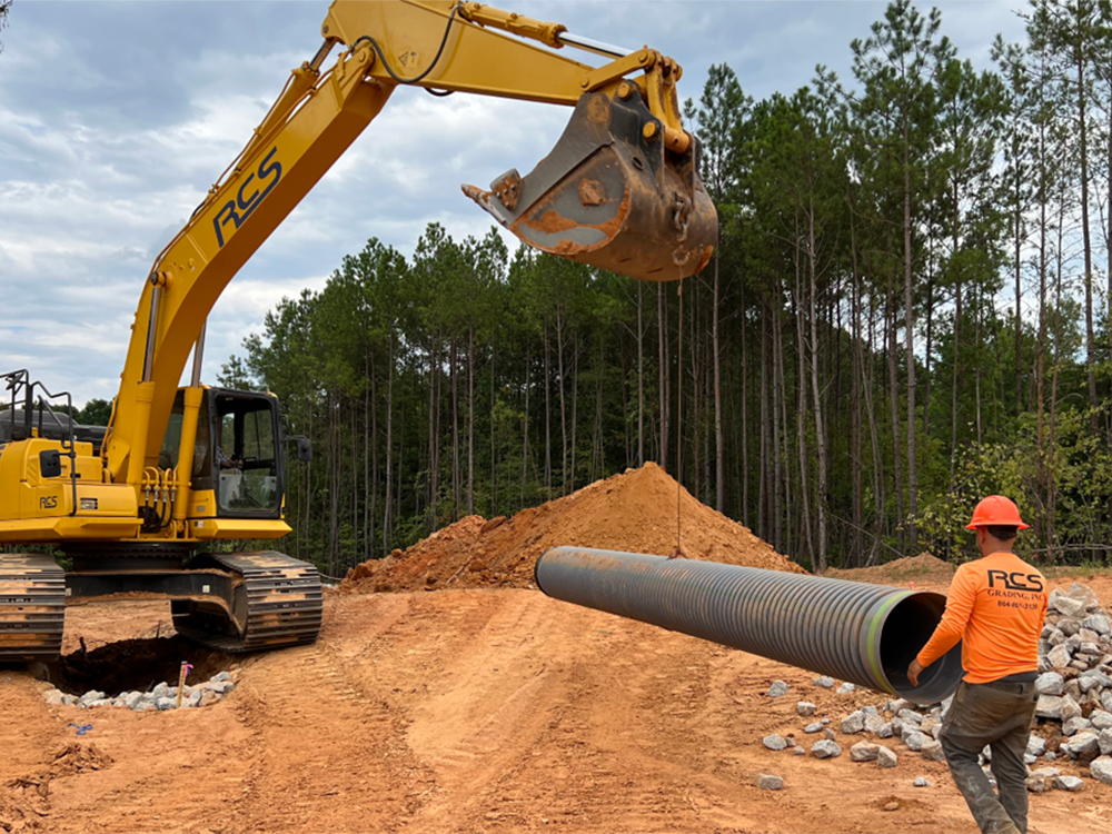 construction worker laying a drainage pipe and directing an excavator
